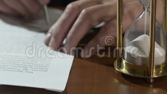 老人阅读和签署生活遗嘱文件沙子在沙漏的桌子上流动视频的预览图