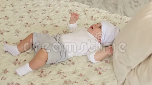 一个刚出生的可爱男孩戴着白色帽子躺在家里的床上视频的预览图