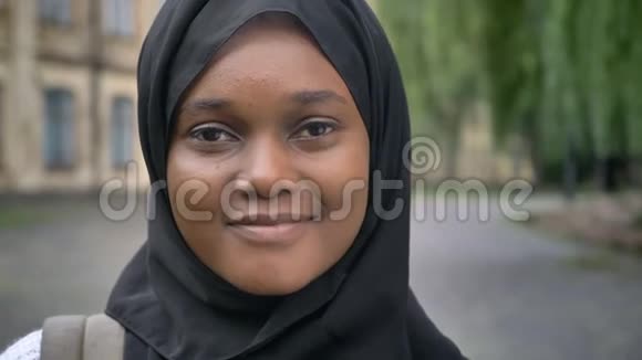 年轻的非裔美国穆斯林女学生戴着头巾对着镜头微笑站在大学附近的公园里视频的预览图