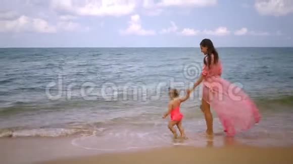 穿着粉红色连衣裙的母女正沿着美丽的海滨散步母亲的概念幸福的童年视频的预览图
