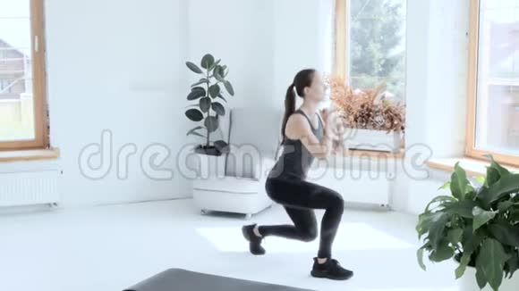 穿运动服的年轻黑发女孩在家做运动做蹲坐视频的预览图