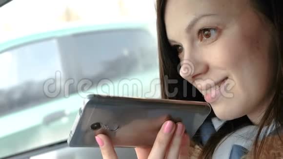 年轻漂亮的女人在坐在车里的手机上说一句语音信息微笑着视频的预览图