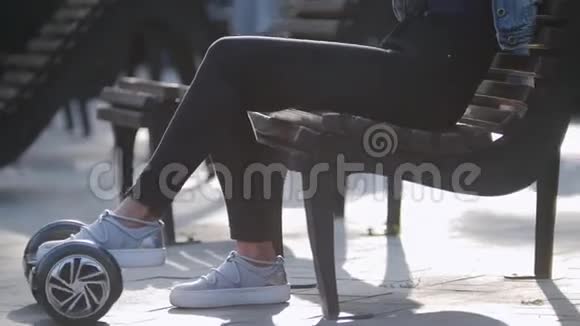 美丽的女孩坐在公园的长凳上看着电话卷着一只脚陀螺视频的预览图