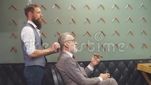 坐在理发店椅子上选择理发设计的胡子老商人视频的预览图