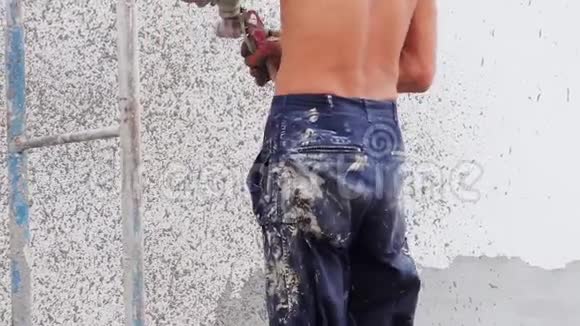 一个男建筑工人用抹灰喷雾器将装饰饰面涂在街道墙上视频的预览图