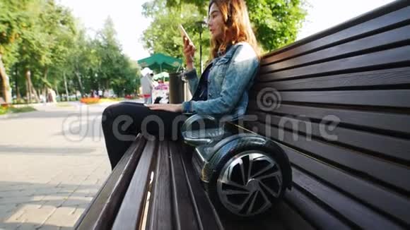 可爱的小女孩坐在公园的长凳上在电话里说话陀螺仪躺在他旁边的长凳上视频的预览图