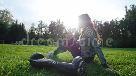可爱的小女孩坐在公园的草地上手里拿着电话通信下一个是陀螺仪视频的预览图