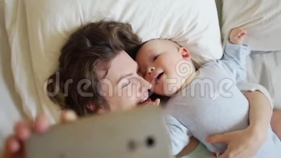 妈妈和宝宝躺在床上自拍宝宝咬妈妈的脸颊快乐家庭周末视频的预览图