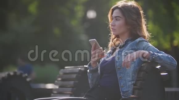 年轻漂亮的女孩坐在长凳上拿着电话一条腿抓着一只陀螺视频的预览图