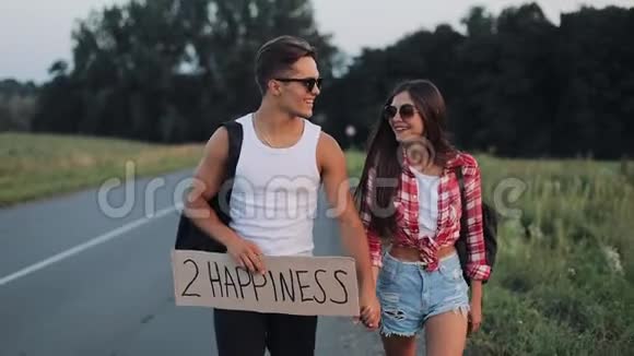 情侣在度假途中搭车手持2个幸福标志夏日时光徒步旅行游客冒险视频的预览图
