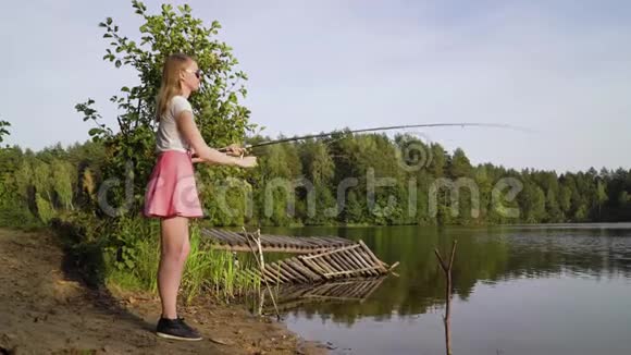 金发少女渔夫正在森林湖上钓鱼拖着钓到一条鱼拿着鱼竿扭动着视频的预览图
