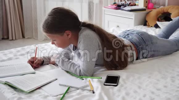 在家学习的小女孩躺在床上写着笔记本视频的预览图