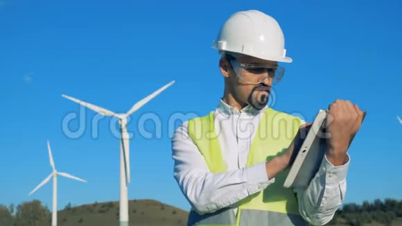 一名男子在风力涡轮机附近的平板电脑上工作绿色能源概念视频的预览图