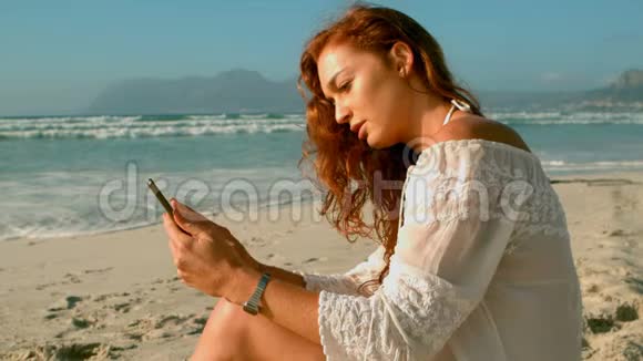 白人女性在阳光下坐在沙滩上使用手机视频的预览图