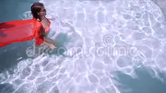 穿着粉红色长裙的女性在水下的蓝色游泳池里游泳粉红色织物在水中发展视频的预览图