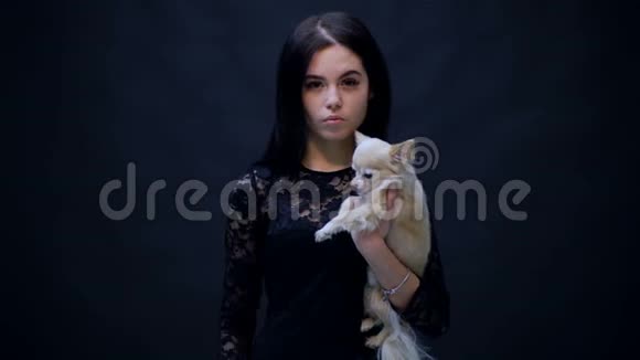 穿着黑色衬衫的女孩把狗抱在黑色的背景上一个抱着小狗的女孩喜欢动物视频的预览图