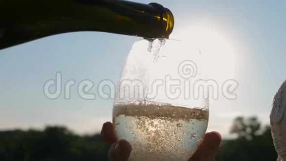 庆祝成功和胜利在夕阳下将瓶中的起泡葡萄酒倒入透明酒杯中视频的预览图