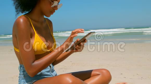 美丽的年轻非洲裔美国妇女在阳光下的海滩上使用数字平板电脑视频的预览图