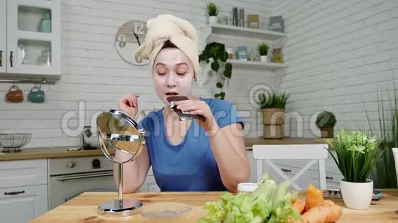 脸上戴面具的亲密女孩坐在镜子里吃巧克力不健康的食物视频的预览图