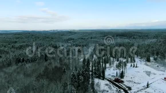 鸟瞰冬季森林两座孤独的房子被蓝色多云的天空背景上的雪树包围运动视频的预览图