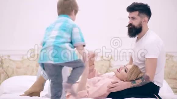 爸爸妈妈和小男孩在床上玩得很开心幸福的家庭在床上拥抱幸福家庭的概念视频的预览图