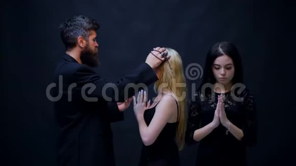 牧师用黑色背景祝福两个女孩崇拜的概念两个穿黑色衣服的女孩承认视频的预览图