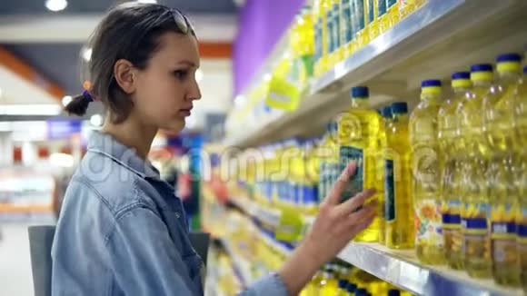 店里的女孩在一个油瓶上看信息贴纸选了一瓶葵花籽油放在手推车上视频的预览图