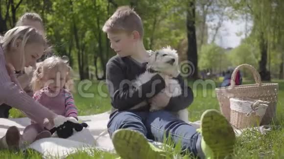 描绘了两个年轻可爱的母亲和他们的孩子坐在绿色惊人的公园的毯子上的自然春天妈妈和视频的预览图