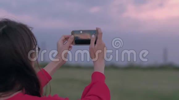 美丽的女人在野外拍摄日落照片使用智能手机视频的预览图