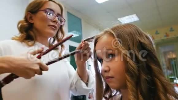 发型师是为小可爱女孩卷发使用电动卷发熨斗关门视频的预览图