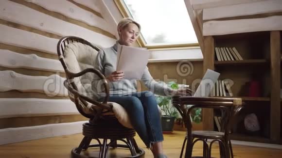 金发短女使用笔记本电脑处理纸质文件视频的预览图