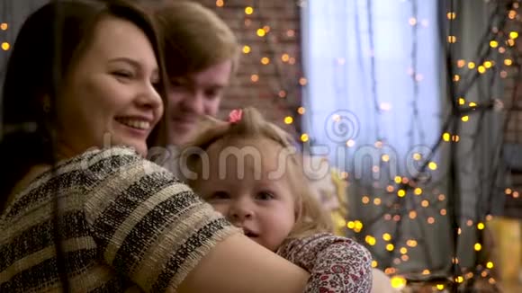 快乐的父母带着微笑的女婴在装饰着黄色花环的房间度过圣诞节父亲母亲和小女儿视频的预览图