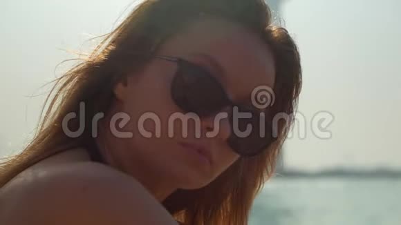 戴着太阳镜的年轻女性正坐在迪拜的公共海滩上笑容满面特写镜头视频的预览图