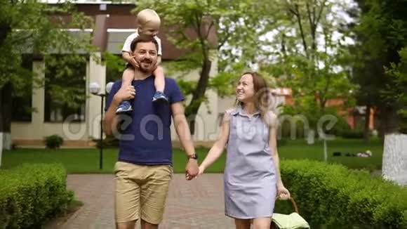 幸福的一家人在阳光明媚的日子里一起走在街道上小男孩骑在父亲肩膀上高加索人视频的预览图