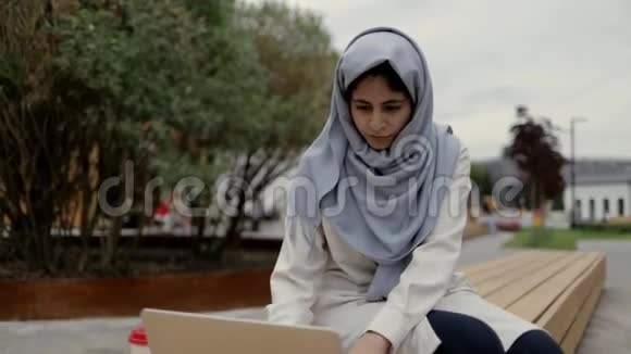 穿着穆斯林传统服装的漂亮年轻女子在外面的笔记本电脑上打字视频的预览图