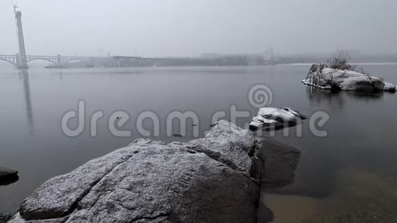 在一个大雪纷飞的阴天静静的河水上的岩石视频的预览图