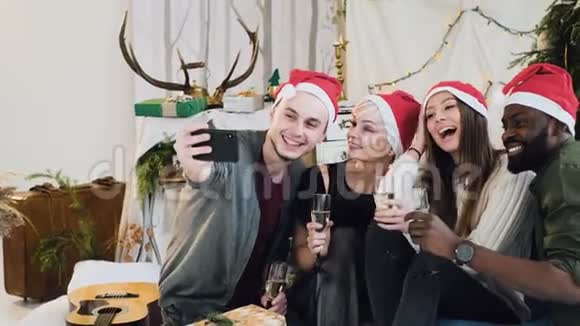 圣诞老人的帽子上戴着圣诞老人帽子的快乐男人和女孩拿着一杯香槟在圣诞节旁边拍自拍照片视频的预览图