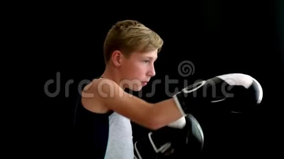 一个十几岁的运动员站在黑暗的背景上他的手戴着黑白手套男孩打了一拳左边视频的预览图
