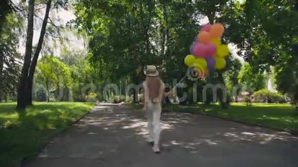 快乐的小女孩在阳光明媚的绿色公园里奔跑手里拿着五颜六色的气球视频的预览图