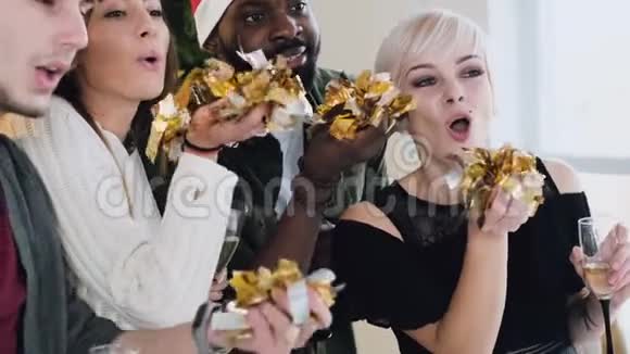 特写镜头不同种族的朋友戴着圣诞帽用手吹着金色的纸屑圣诞节和新年视频的预览图