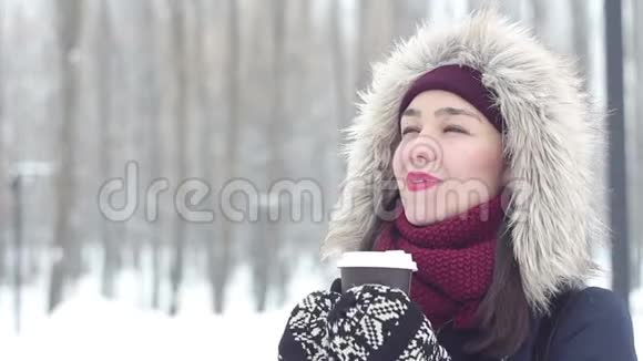 美丽的少女端着一杯咖啡用呼吸温暖双手行走在冬林中视频的预览图