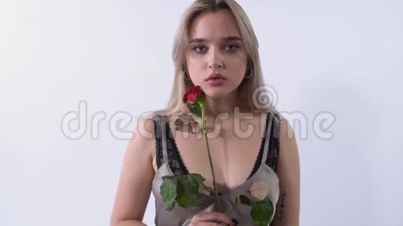 一幅孤独的女孩的肖像穿着刺鼻站在一个明亮的工作室的白色背景上玫瑰花瓣倒在上面视频的预览图