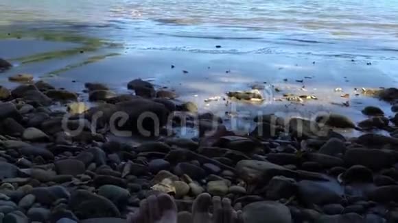年轻女子的腿在石头海滩上在阳光明媚的日子里海浪拍打着海岸视频的预览图