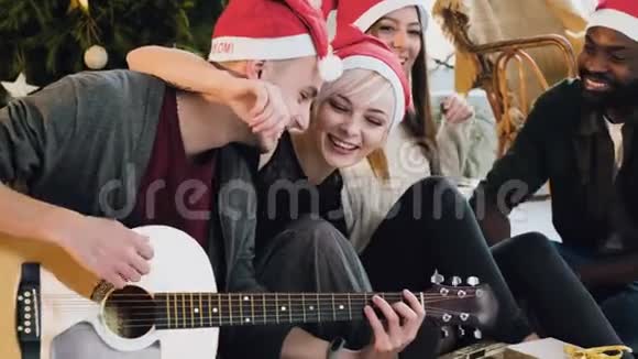 一群年轻漂亮的人在圣诞节装饰的背景下拥抱并弹吉他视频的预览图
