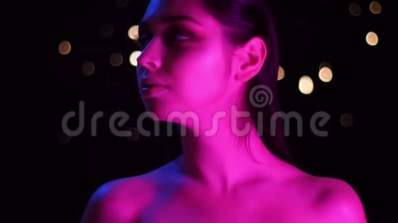 在镜头前摆着粉色霓虹灯和bokeh背景的年轻白种人女性特写镜头视频的预览图