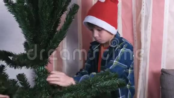 和妈妈一起戴圣诞帽的快乐男孩在家里安装圣诞树为圣诞节做准备视频的预览图