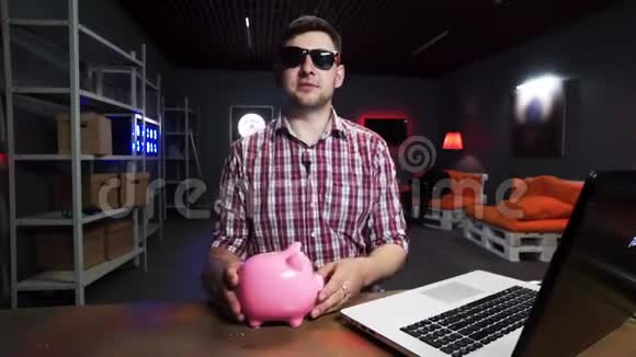 戴着墨镜的可爱胡须男抱着塑料猪说话看着镜头视频的预览图