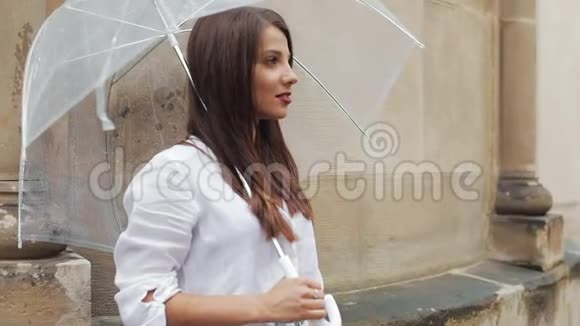 在城市里微笑的女人在伞下看着侧面的肖像她站在商业附近的街道上视频的预览图