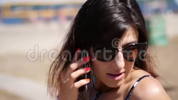 肖像美丽的女孩戴着太阳镜的女人在手机上说话在海滩上在炎热的夏天视频的预览图