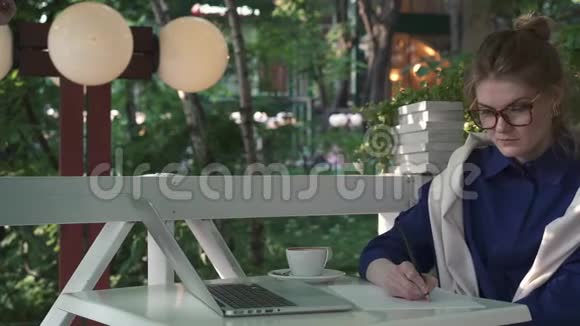 严肃的高加索女商人在夏天的咖啡馆里写作业务战略视频的预览图